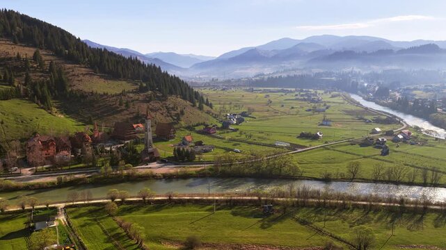 Aerial drone view of Dorna Valley near Vatra Dornei, Romania, featuring a winding river, green pastures, and scattered farms