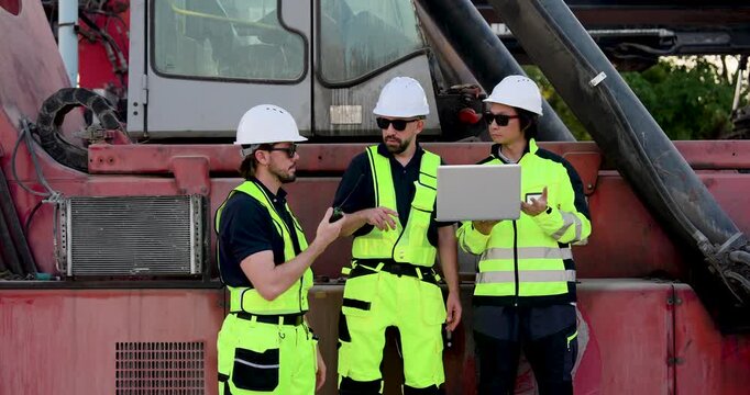 Adult Caucasian logistics group coordinate near reach stacker, using radio and laptop for freight operation, container handling safety, cargo dispatch, yard workflow and shipment control plan