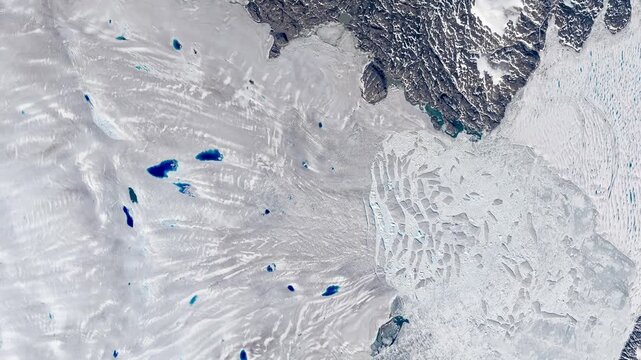 Top shot on glacier flowing into sea, cracking in pieces making icebergs. Camera is moving backward and right. Animation based on image by NASA