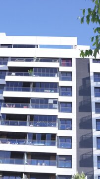A daytime low-angle vertical shot of the iconic Mirador building in Madrid, Spain. The contemporary residential tower features high-contrast white, dark grey, and red panels with a massive open centra