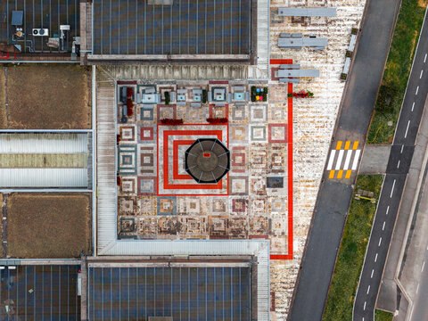 Aerial view of a modern building rooftop featuring geometric patterns and a central octagonal structure with a nearby road in Leccio, Toscana, Italy.