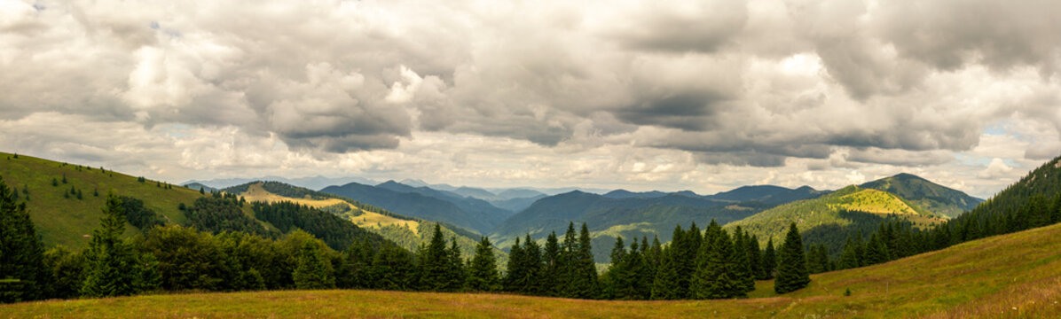 Expansive panoramic view of rolling green hills and mountain ridges with dramatic cloudscape and sunlit meadows