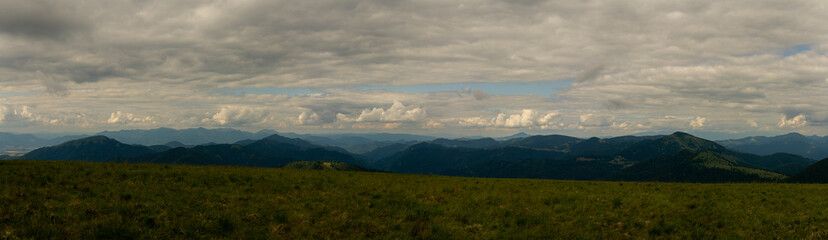Obraz premium Majestic panoramic view over rolling green mountain ridges under dramatic cloudy sky in summer daylight landscape