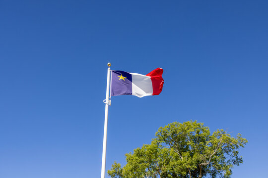 Acadian flag flying on a white flagpole against a clear blue sky in Nova Scotia Canada celebrating Acadian heritage and cultural identity.