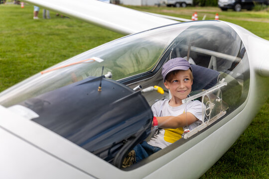 Cute little happy boy sits inside glider cockpit aviation club activity airfield. Childhood dream flying flight school experience, inspiring curiosity, learning, adventure and future aspirations