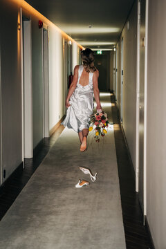 Runaway barefoot bride escaping hotel hallway with wedding dress