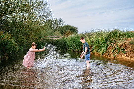 Sister splashing water toward her brother in a summer stream