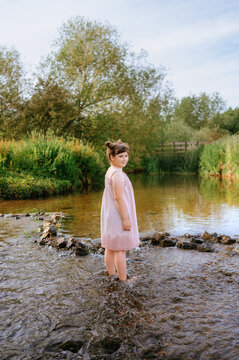 oung girl standing in shallow stream surrounded by nature