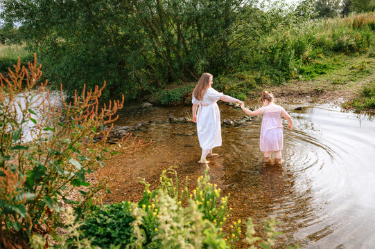 Mother and daughter walking through shallow stream in countryside