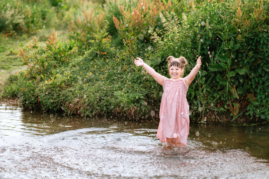 Child girl raising her arms while playing in a stream