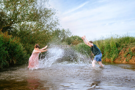 Brother and sister splashing water at each other in a stream