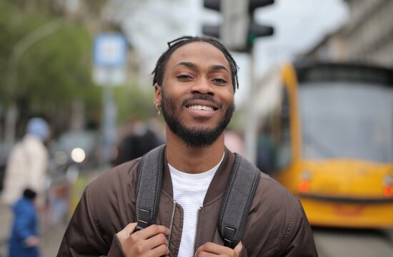 Confident young Black man with backpack smiling in city