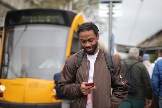 Young Black man looking at his smartphone at a tram stop