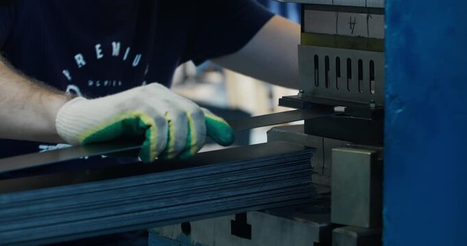 Close-up of industrial worker hands handling metal components at stamping machine. Detailed factory production process
