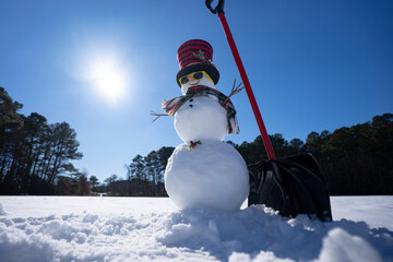 Fototapeta premium Winter design with snowman and snow shovel. Winter snowman with shovel clearing snow outdoors. Winter outdoor scene with snowman. Cute snowman with snow shovel and wooden vintage sled in winter field.