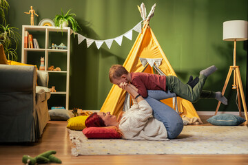 Mother lying on floor lifting son in playroom © MexChriss