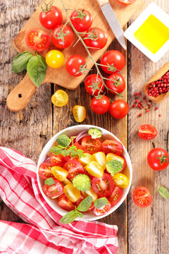 fresh cherry tomato salad with broccoli and basil in bowl on rustic wooden table top view