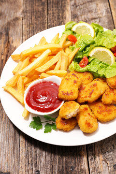 chicken nuggets with french fries, ketchup sauce and green salad on plate with wooden background
