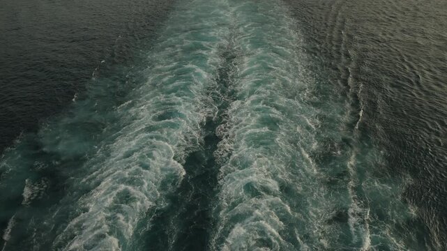 Twin white foaming wake trails cut through dark choppy green ocean surface seen from ship deck above