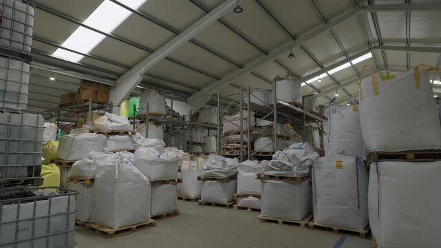 Wide recycling warehouse interior packed with rows of white bulk bags on wooden pallets under steel roof