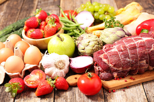 raw beef roast with fresh vegetables, fruits and eggs on rustic wooden table