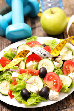 fresh salad with measuring tape dumbbells and apple on rustic wooden table fitness and diet concept
