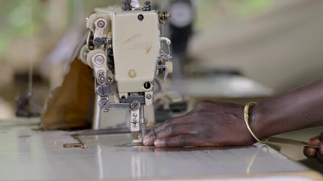 Close up footage showing a tailor&rsquo;s hands guiding fabric through a fast moving electric sewing machine. Detailed textile craftsmanship and garment production in a tailoring workshop.