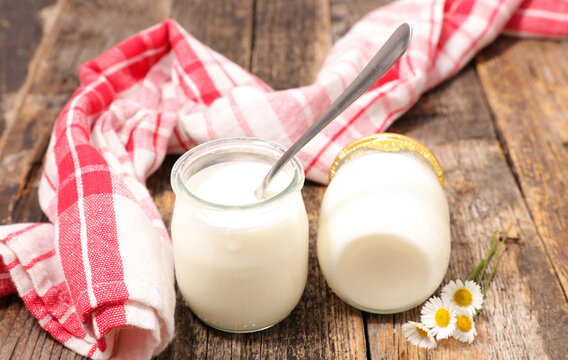 fresh yogurt in small glass jars with spoon and red checkered napkin on rustic wooden table