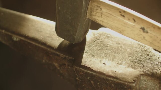 Close-up of an iron hammer with a wooden shaft resting on an anvil, highlighting rustic craftsmanship and blacksmithing details.
