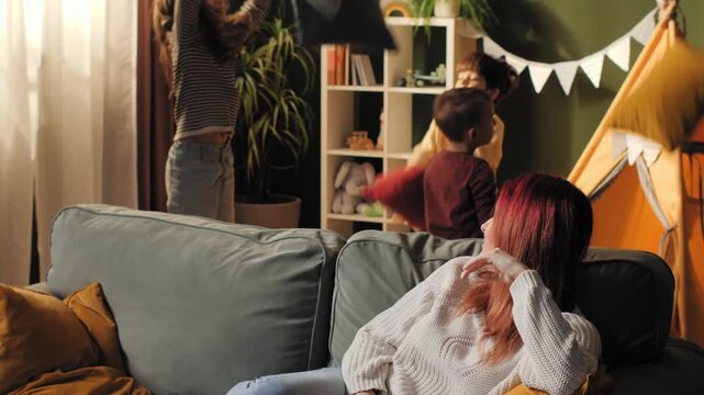 Exhausted mother ignoring playing children in living room