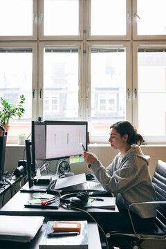 Female corporate professional using smart phone while working at desk in tech office