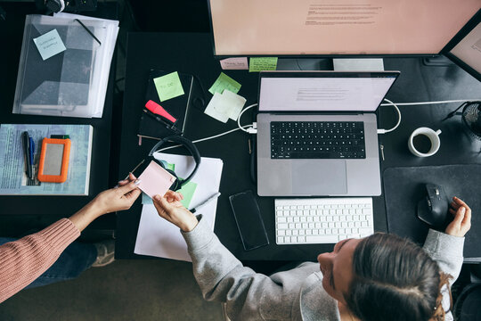 Directly above view of female entrepreneur passing adhesive note to colleague while sitting at desk in office