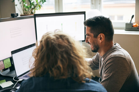 Happy male tech expert working with colleague on multiple devices in startup office