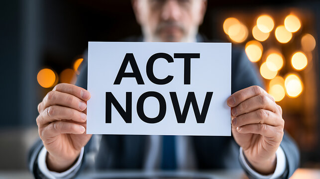 Professional presenting 'ACT NOW' sign, urging immediate decision and action in a blurred corporate setting