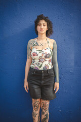 Fototapeta premium Confident tattooed woman standing in front of blue wall