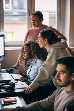 Multiracial female tech experts analyzing details on computer while working in startup office