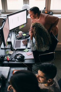 High angle view of multiracial female tech experts comparing responsive design preview on dual monitor in startup compan