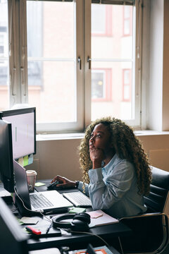 Concentrated female business professional analyzing data preview on dual monitor in startup office
