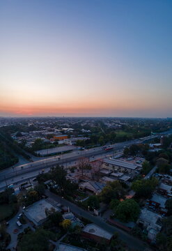 Aerial view of the urban landscape featuring the Arfa Kareem Tower at sunset with a busy highway, residential rooftops, and lush green trees in Lahore, Punjab, Pakistan.