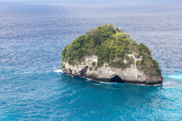 Obraz premium Rocky island with sea cave and green trees in turquoise ocean at Diamond Beach, Nusa Penida, Bali, Indonesia coastal scenery.