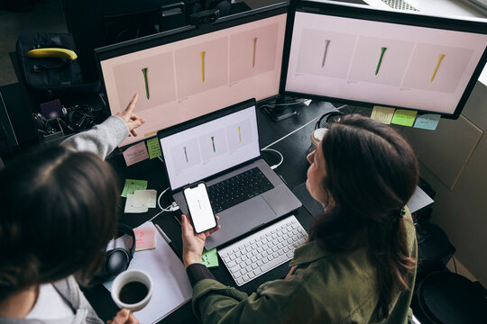 High angle view of businesswoman sharing ideas with coworker while comparing design preview on devices in office
