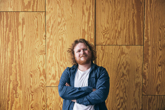 Portrait of confident male tech entrepreneur standing with arms crossed against brown wall in office