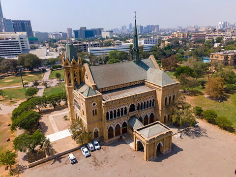 Aerial view of Frere Hall, a historic building with Gothic-Venetian architecture, surrounded by lush green gardens and the urban skyline in Karachi, Sindh, Pakistan.