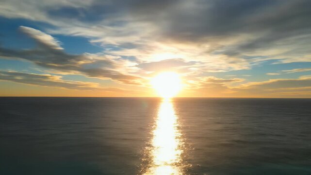 Sun sets over a calm ocean horizon, casting a golden path on the water