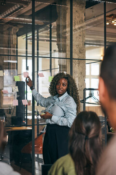 Female tech professional explaining business ideas through adhesive notes to team during meeting in office