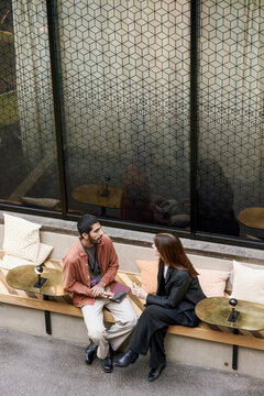 High angle view of male entrepreneur talking with female associate at meet and greet event while sitting on bench in con
