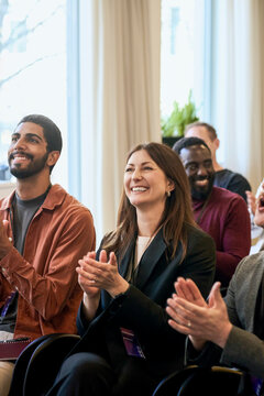 Smiling businesswoman clapping while attending seminar with colleagues in convention hall