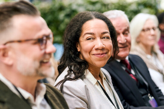 Smiling mature female entrepreneur attending seminar with male colleagues in convention center