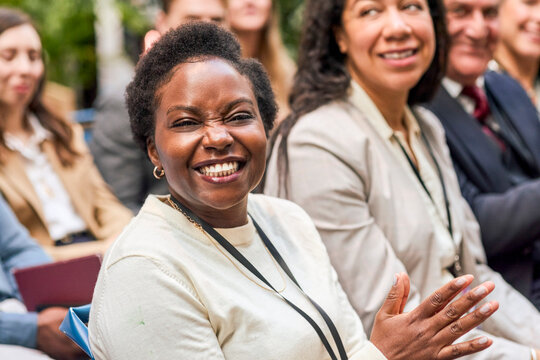Portrait of short haired female business professional with toothy smile clapping during session in convention center