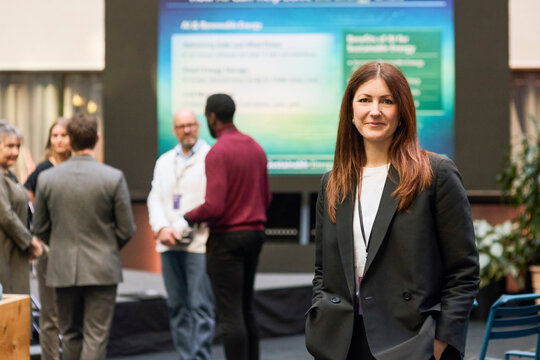 Portrait of female business professional wearing blazer standing with hand in pocket at convention center
